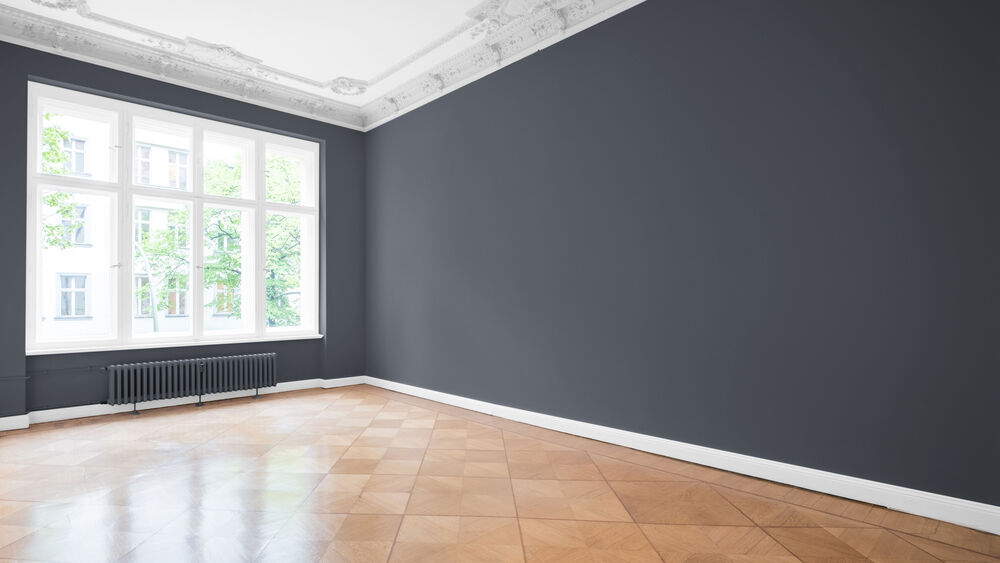 An empty room, big window, wooden floor and freshly painted dark grey walls.