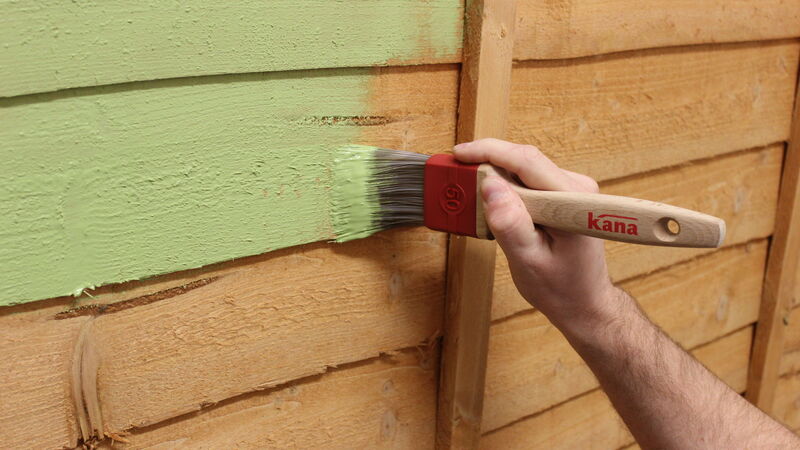 IMG_7503 Closeup of a wooden fence being painted with a paint brush.